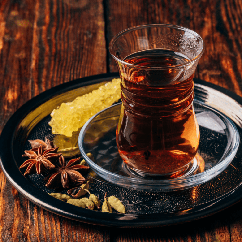 Spiced tea in oriental glass with star anise and green cardamom on metal tray over wooden surface. Concept of Ayurvedic remedies and practices applied to modern life by Gyana