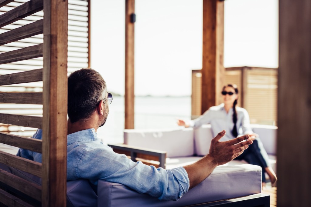 Business mentoring session in an open air in wooden patio, where a businessperson talks in a relaxed atmosphere with a woman, discussing business coaching, ancient business practices and application in modern life for success and realization of goals.