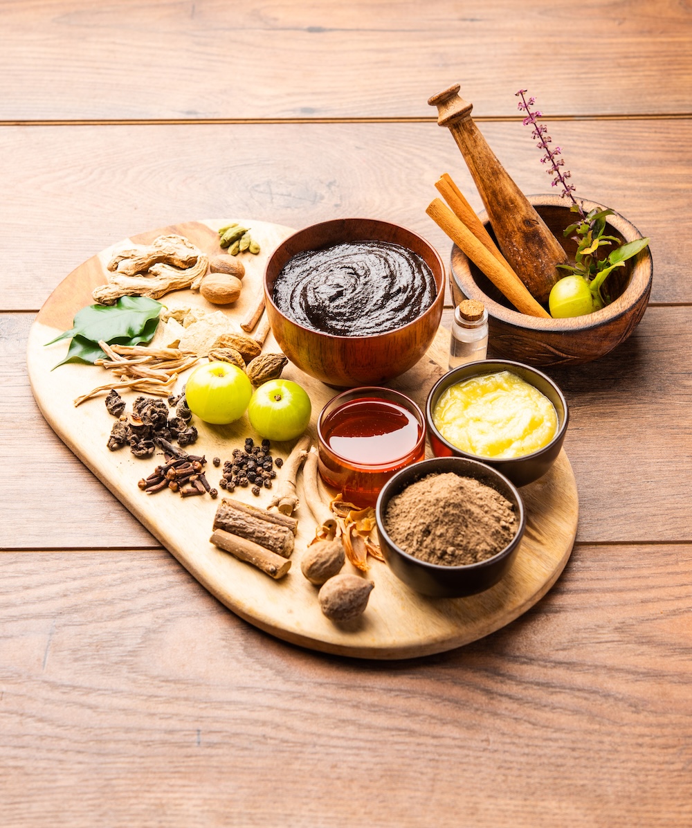 A wooden tray with Chyavanprash or chyawanprash - an ayurvedic rasayana for wellbeing, praised in Charaka Samhita and usefulf for modern living. Ayurvedic spices like amla, ginger, long pepper, curry leaves, cardamon, ashwagandha roots, honey and ghee are lying on the tray - these are some of the chawanprash ingredients