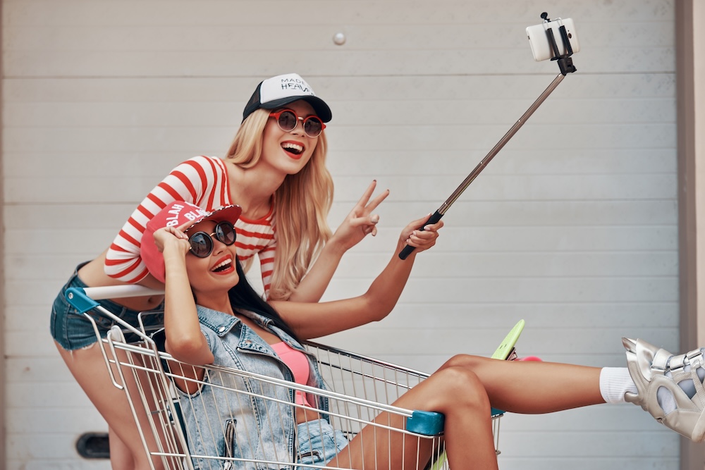 Two happy young women making selfie on smart phone while having fun together outdoors. The social media concept amd how it is impacting daily life and wellbeing