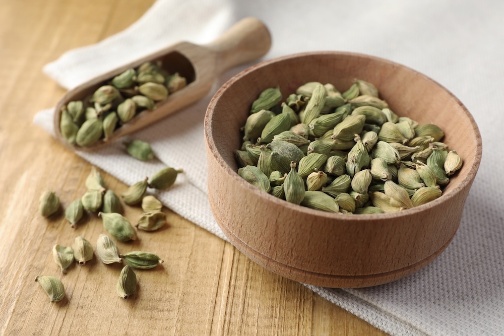 Bowl and scoop of dry cardamom pods on wooden table, elachi: perfect cooling ayurvedic spice, blood pressure remedy, digestion facilitator