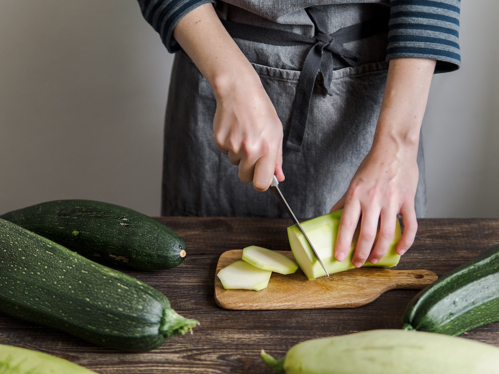 Zucchini harvest. Woman slices zucchini on wooden table. Farm organic summer squash, zucchini harvesting. Ayurvedic summer squash, zucchini preparation, recipes and benefits for health.