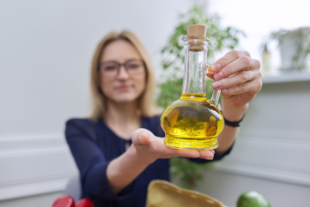 Olive oil in bottle in hand of woman nutritionist, healthy food, healthy lifestyle. Concept of Ayurvedic properties, benefits of olive oil, and how to find out if olive oil is fake.