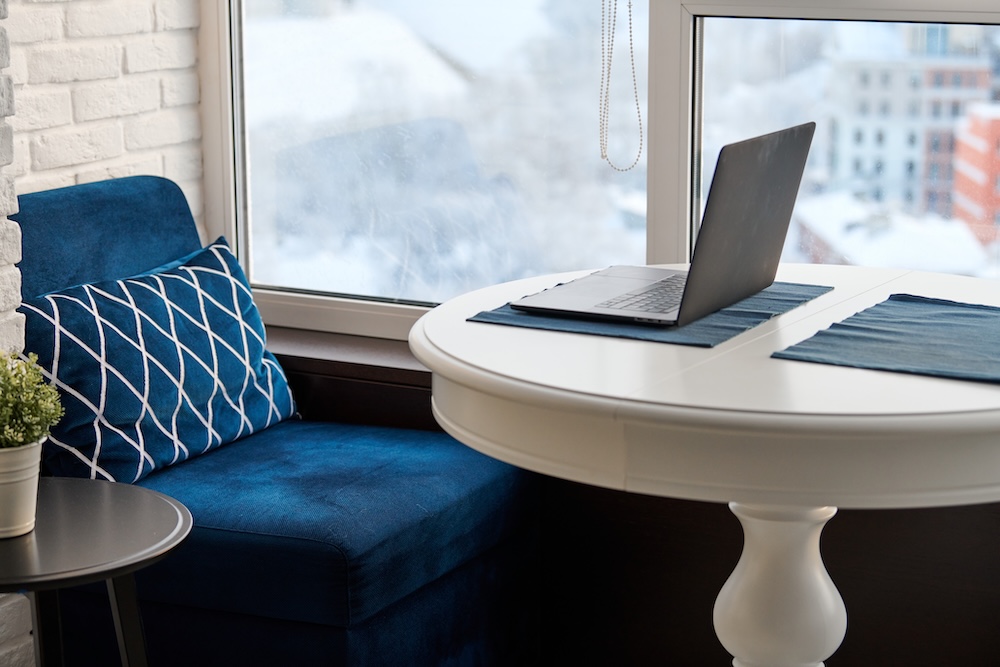 Home workplace in modern loft apartment. Laptop on white table, cityscape in window background. Cozy work at home. Vastu spatial design concept, ancient way to organise work space