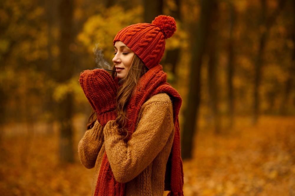 Headshot portrait of young woman drinking steamed hot ayurvedic herbal tea in autumn park. Concept of warming up in cold weather using vedic wisdom and Aryuveda.