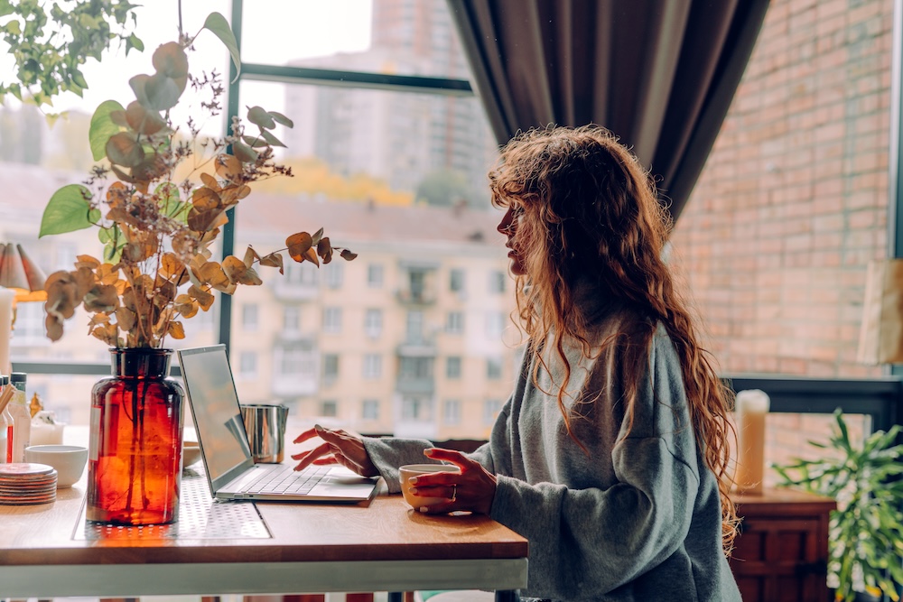 Business woman with curly hair working at the cafe remote office using laptop. Autumn work from home, WFH concept, Vastu ancient principles of spatial design, workplace organizing and well-being.